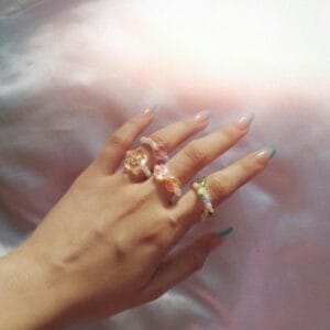 Close-up of a woman's hand adorned with colorful, stylish rings against a silky background.