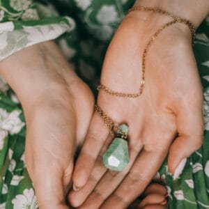 Close-up of woman holding a green crystal necklace, showcasing elegant hands and jewelry details.