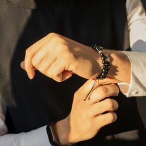 Close-up of hands adjusting a beaded bracelet in warm sunlight, showcasing elegance and style.